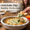 Bubbly spinach artichoke dip in a round baking dish with melted pepper jack cheese, being scooped with a pita wedge alongside crackers and fresh vegetables.