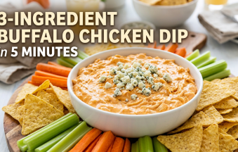 A white bowl filled with creamy orange buffalo chicken dip topped with blue cheese crumbles, surrounded by tortilla chips, celery sticks, and carrots on a wooden platter with bold text reading "3-Ingredient Buffalo Chicken Dip in 5 Minutes".